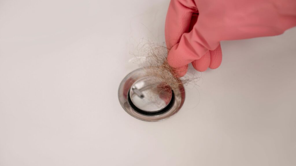 A woman who learned the importance of drain cleaning removes hair from her sink